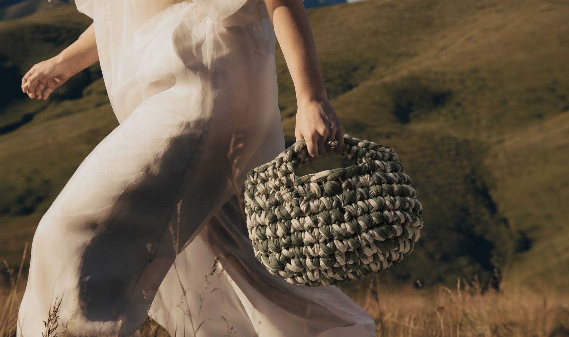 Woven crochet bag carried through a sunlit field